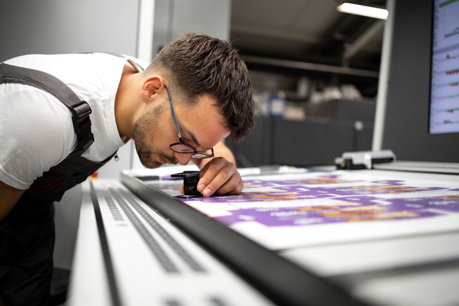 Print technician examining a color sheet with a magnifier at a printing press